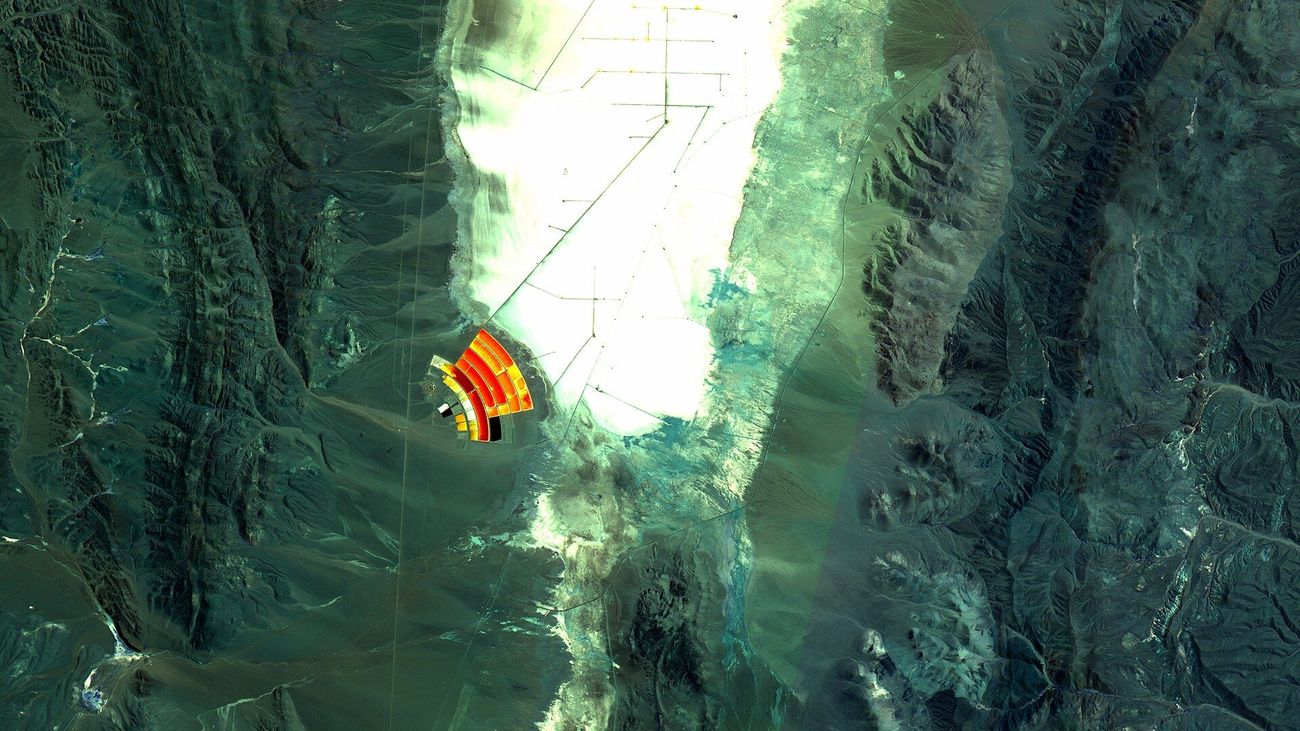 Satellite image of a white salt flat between mountains, with a fan of brightly colored evaporation ponds