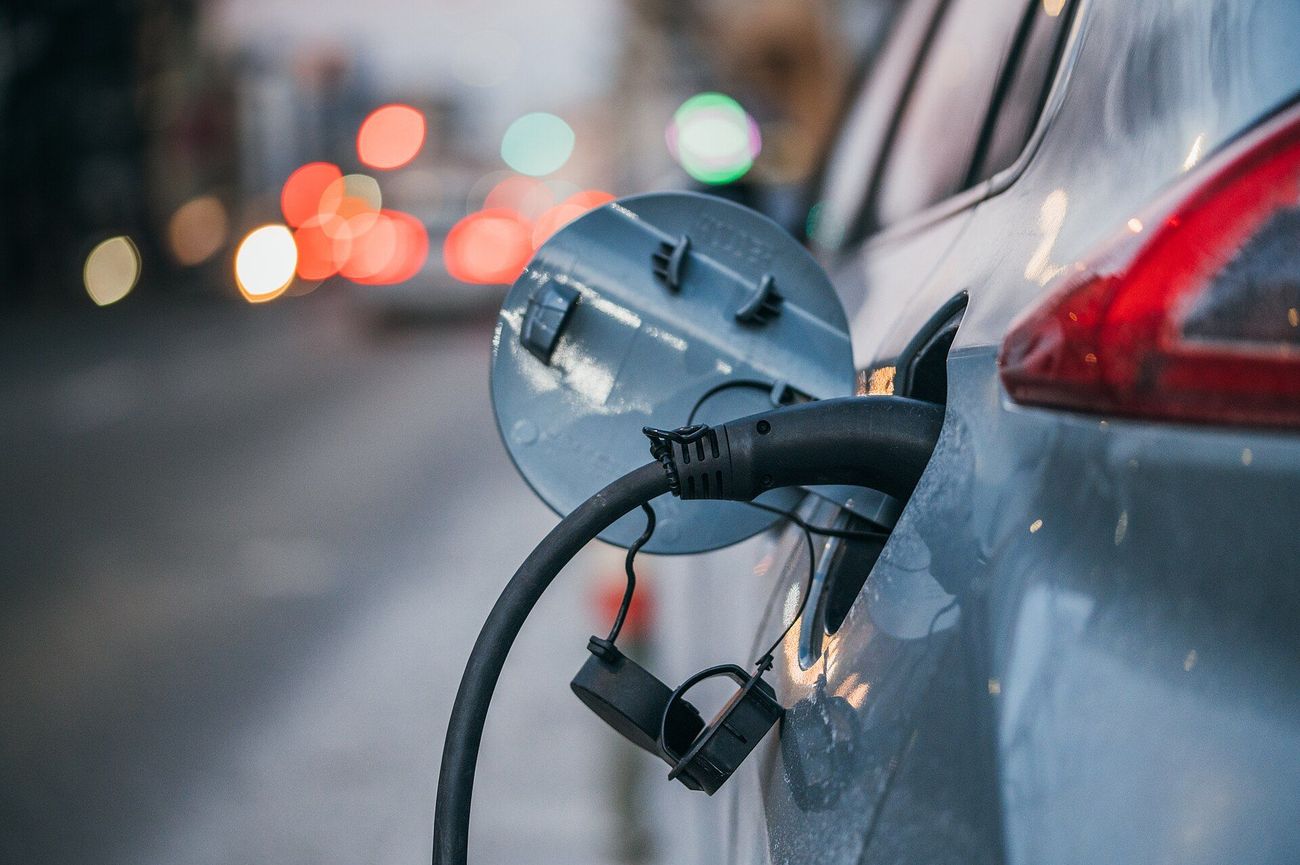 Close-up of a charging cable plugged into an electric car, with city traffic lights blurred behind