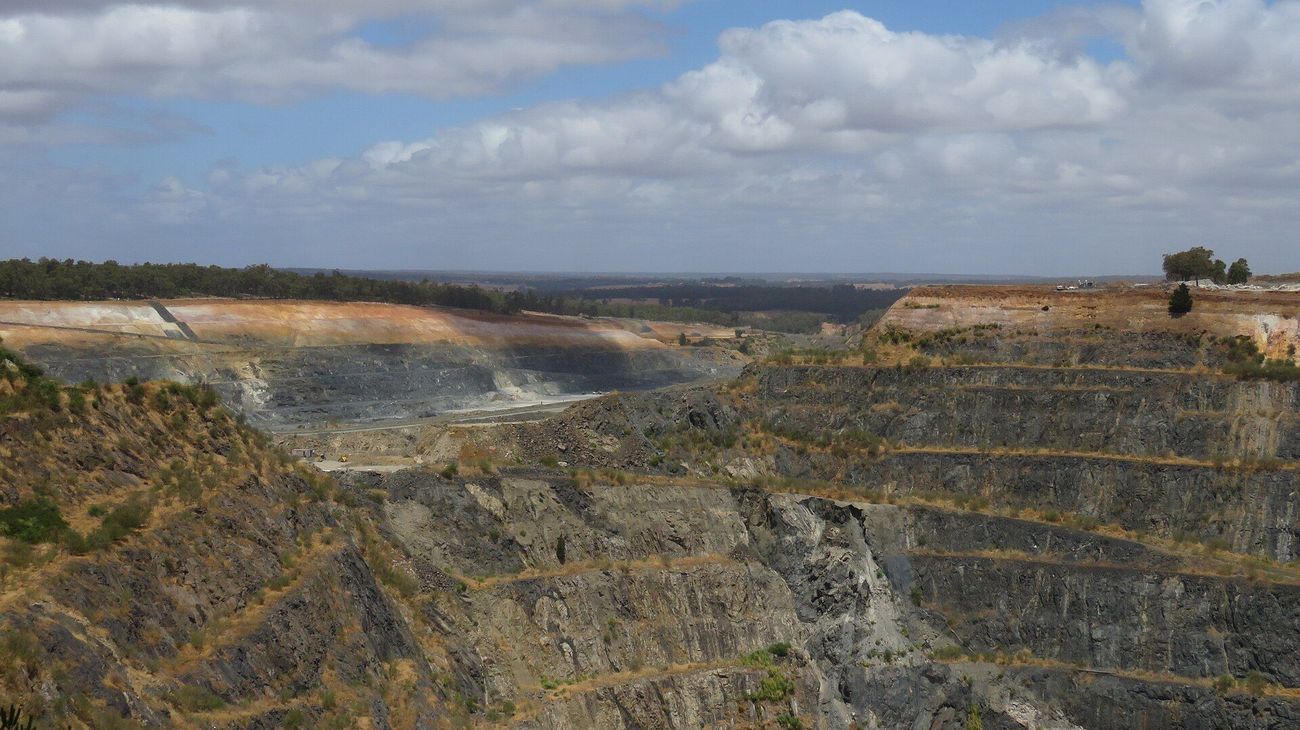 Terraced open pit of the Greenbushes lithium mine in Western Australia under a cloudy sky