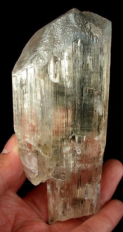 A large translucent spodumene crystal held in a hand against a black background